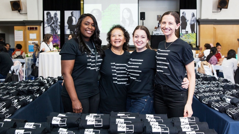 4 women pose for a photo at a table filled with UCSF Campaign t-shirts