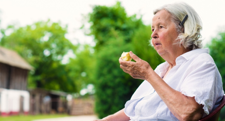 senior woman eating an apple while sitting outdoors