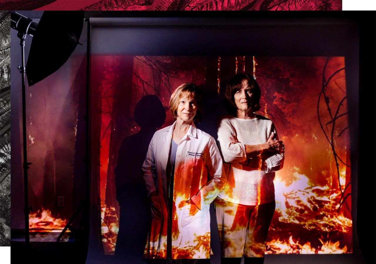Portrait of Dr. Katherine Gundling and Dr. Wendy Max in a photo studio setting with a projection of a forest fire.