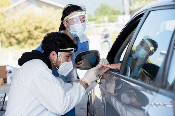 Two clinicians taking blood from a patient's hand held out of car window
