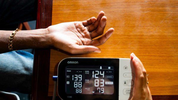 A close-up shot of a person’s arm extended as a health practitioner measures their blood pressure with an at-home blood pressure monitor.