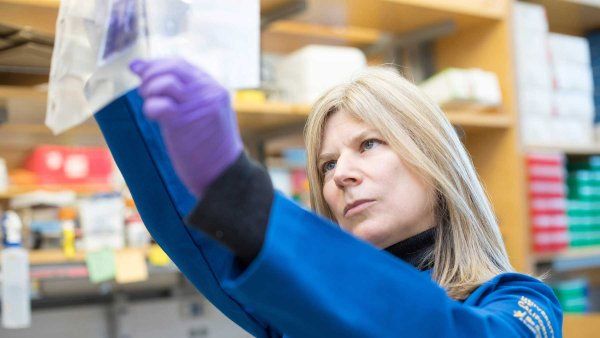 Researcher Tanja Kortemme wears a blue lab coat and purple latex gloves as she examines equipment in her lab.