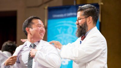John Davis MD, PhD, associate dean for curriculum in the School of Medicine, gives Daniel Kim his white coat during the school’s white coat ceremony.
