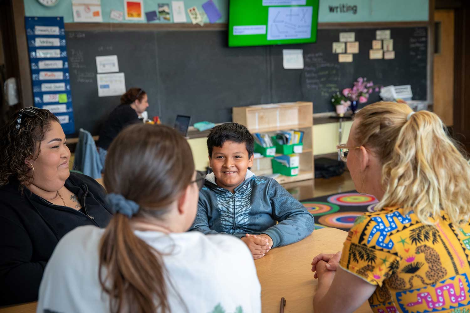 Andrew with his mother, teacher, and social worker Jeannette Feddes meet in a classroom. They smile as they discuss his involvement in the Collaborative Life Skills program.