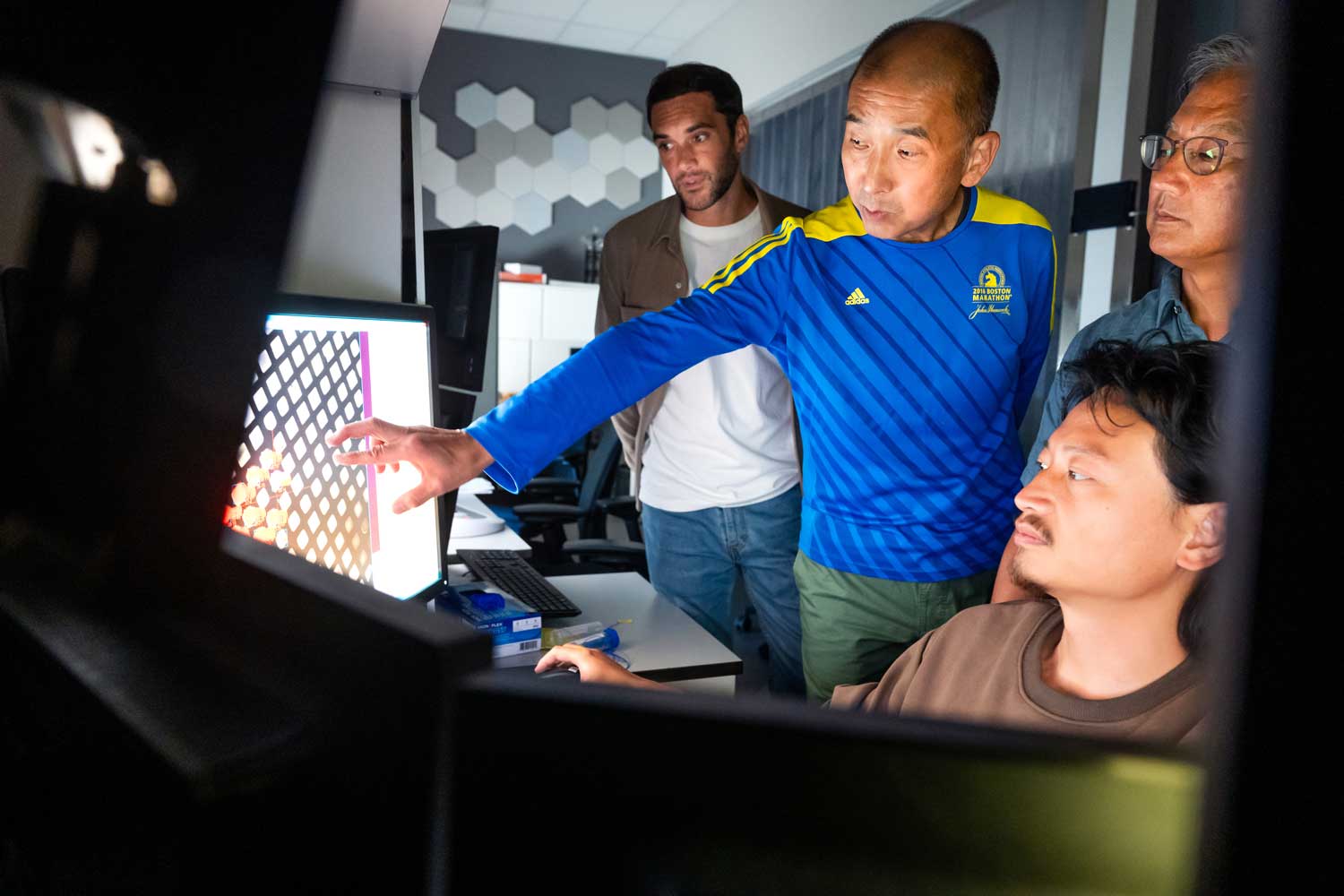 A group of researchers, including Yifan Cheng and Stephen Nishimura, crowd around a computer to look at a Cyro-EM sample.