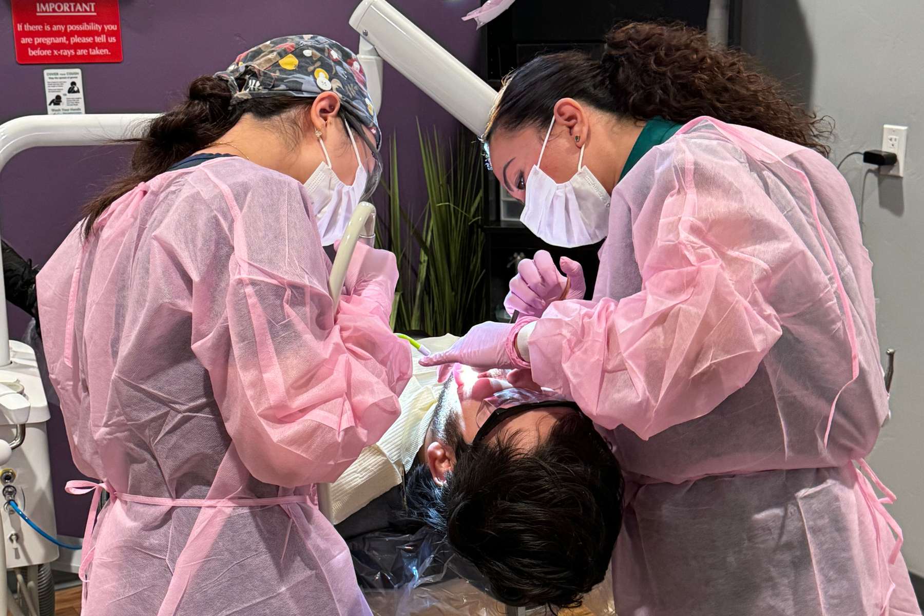 two uniformed students review a patients mouth in chair.