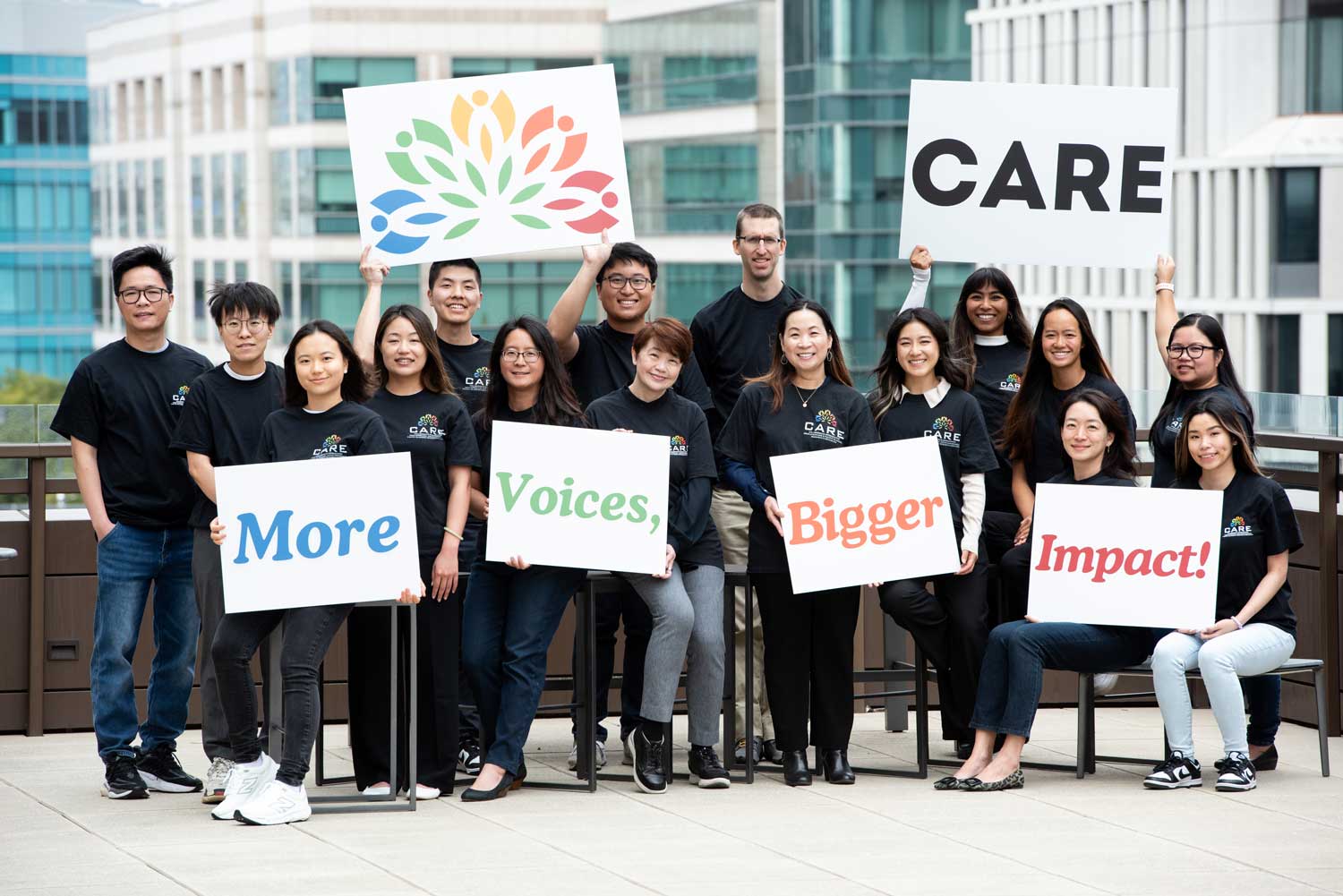 A group photo of the CARE team, who all wear CARE T-shirts and hold up signs that read "CARE" and "more voices, more impact."