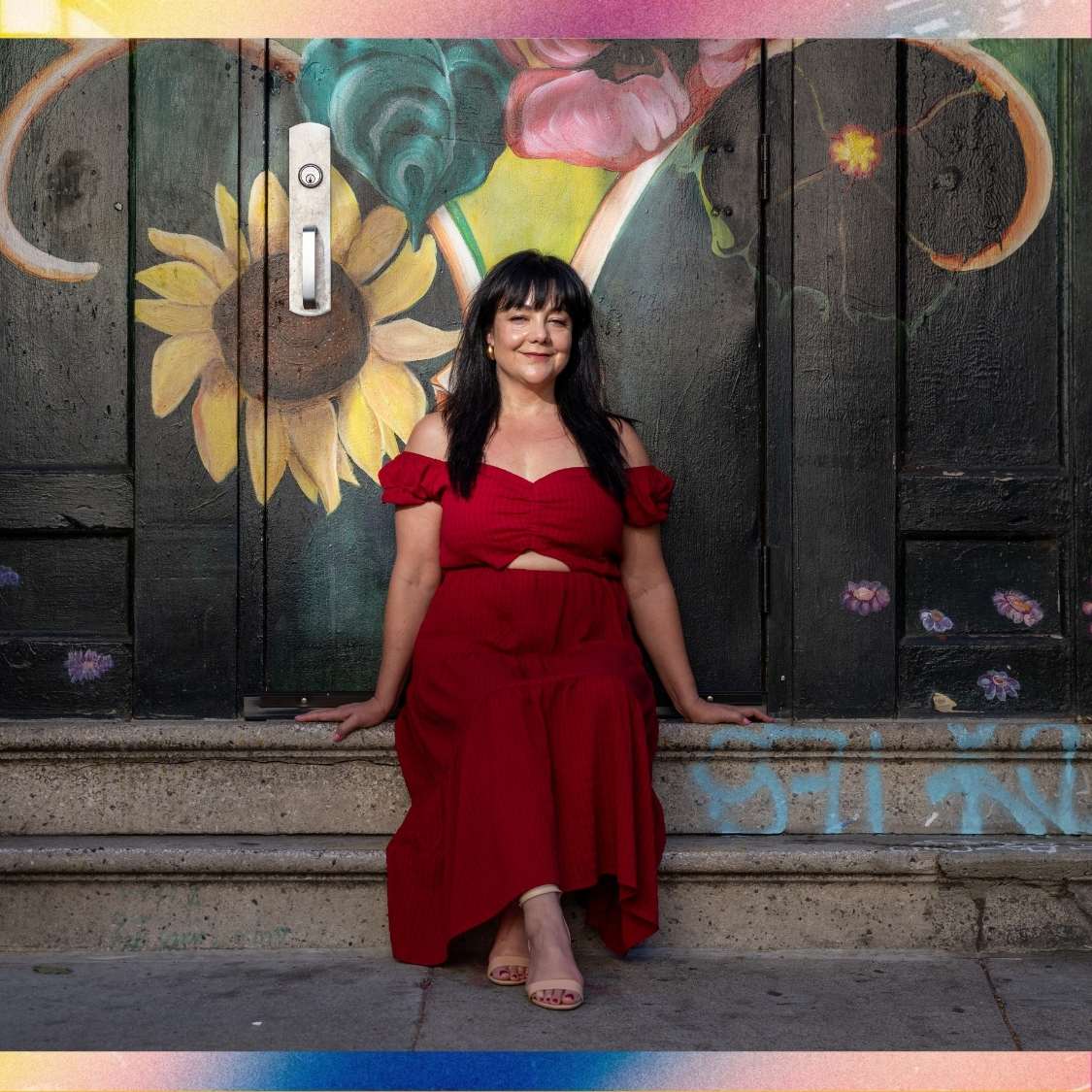 Sophia in red dress sits on steps with mural in background.