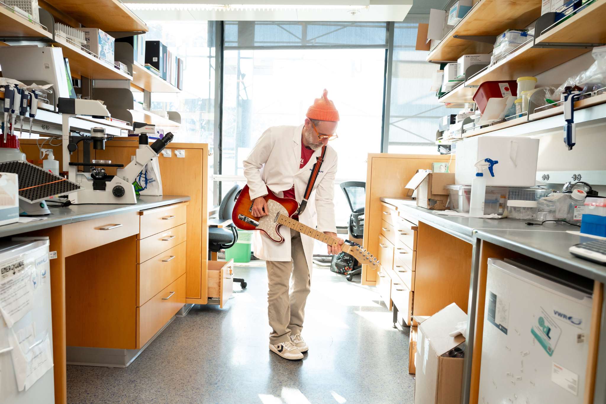 Man plays guitar in laboratory, blending science and music.