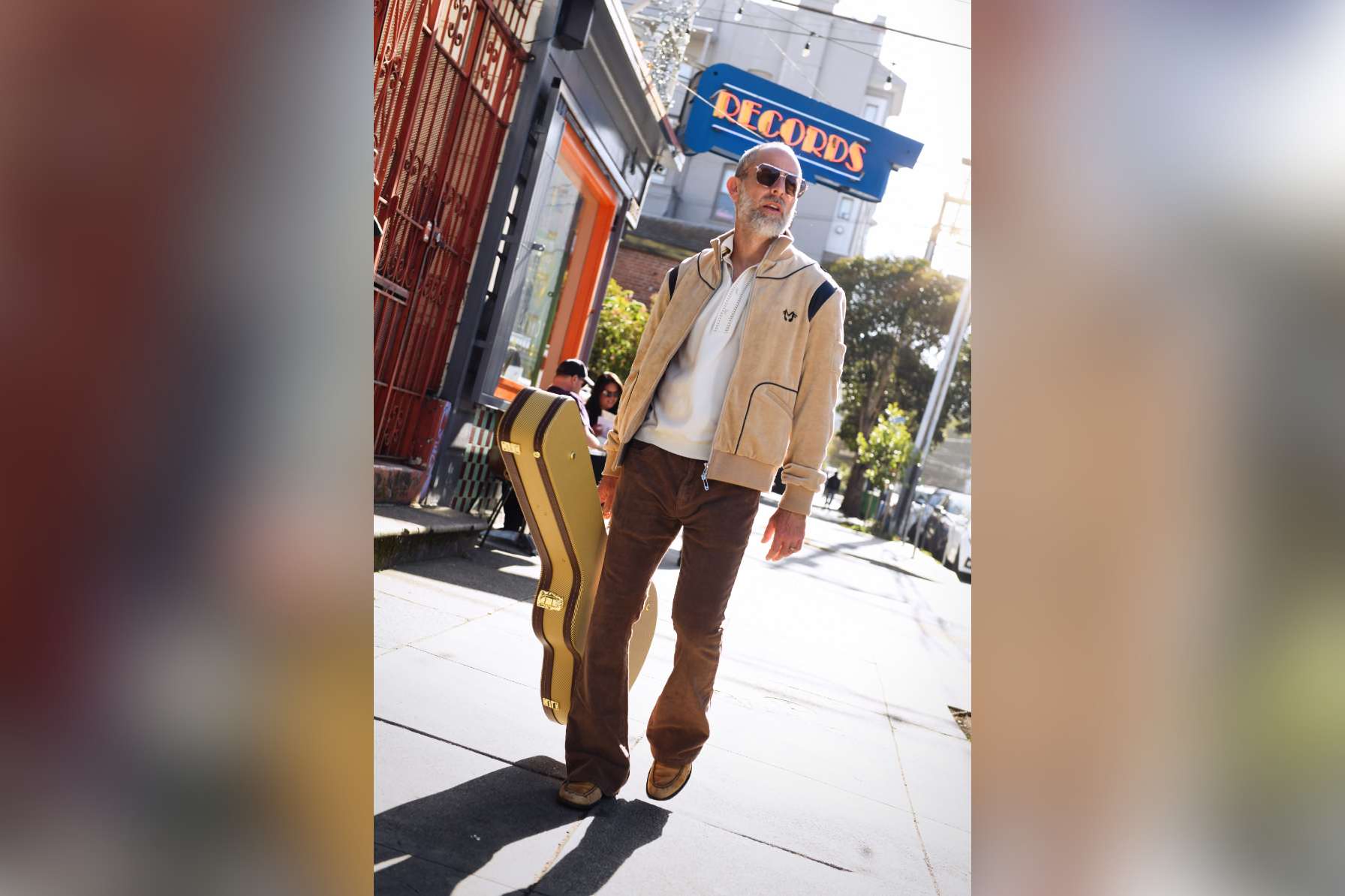 Hip man walks in front of theater holding guitar case.