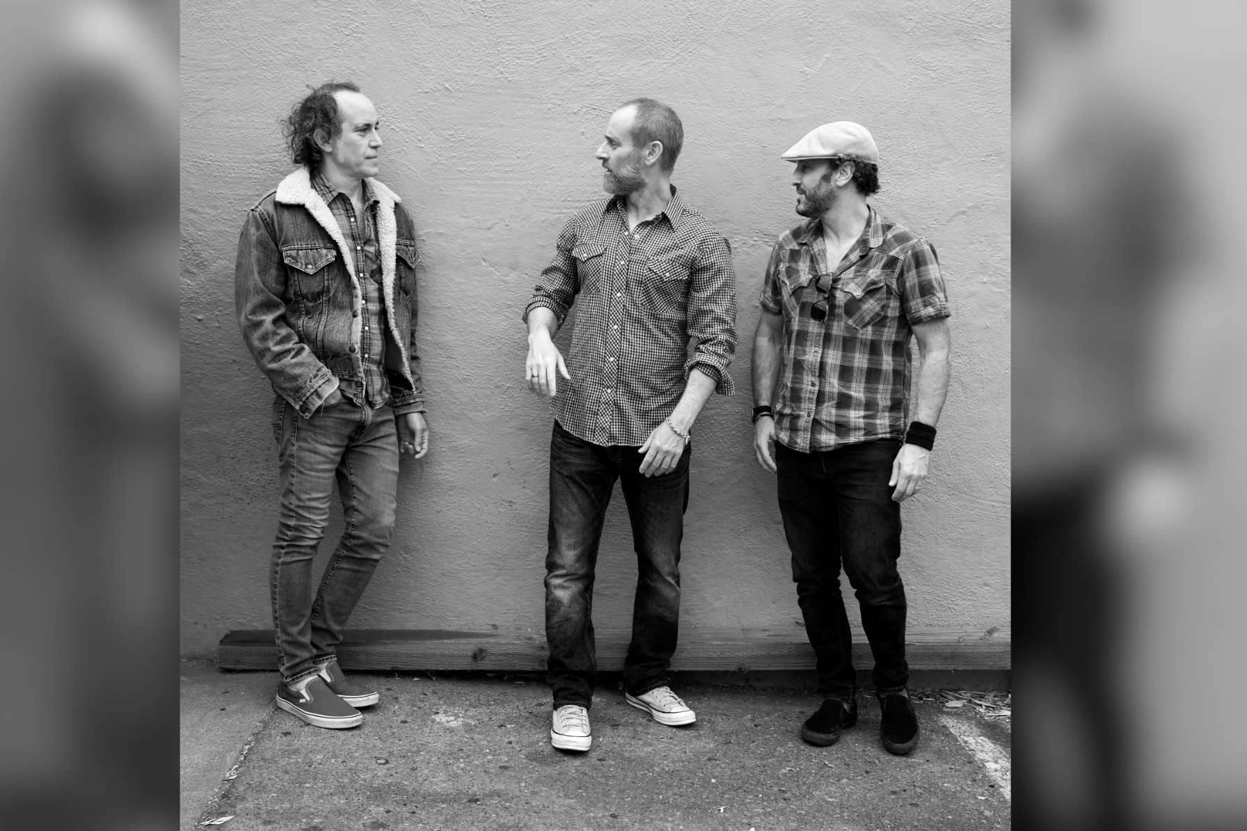 Three hip well-dressed men connect and pose against wall.