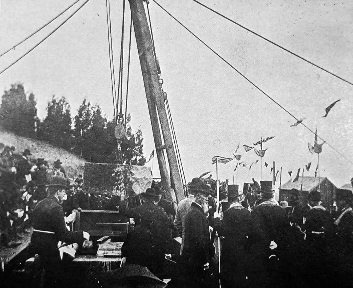 A black and white photo of the groundbreaking of the Parnassus Heights campus. The original building's cornerstone is being laid by workmen while a crowd watches.