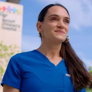 Kathleen smiles with hospital in background.