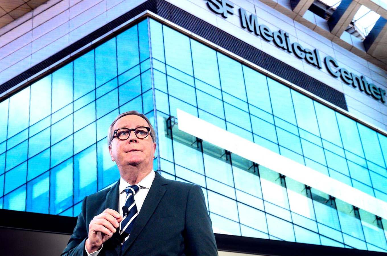 Chancellor's Sam Hawgood speaking with large hospital image behind him.