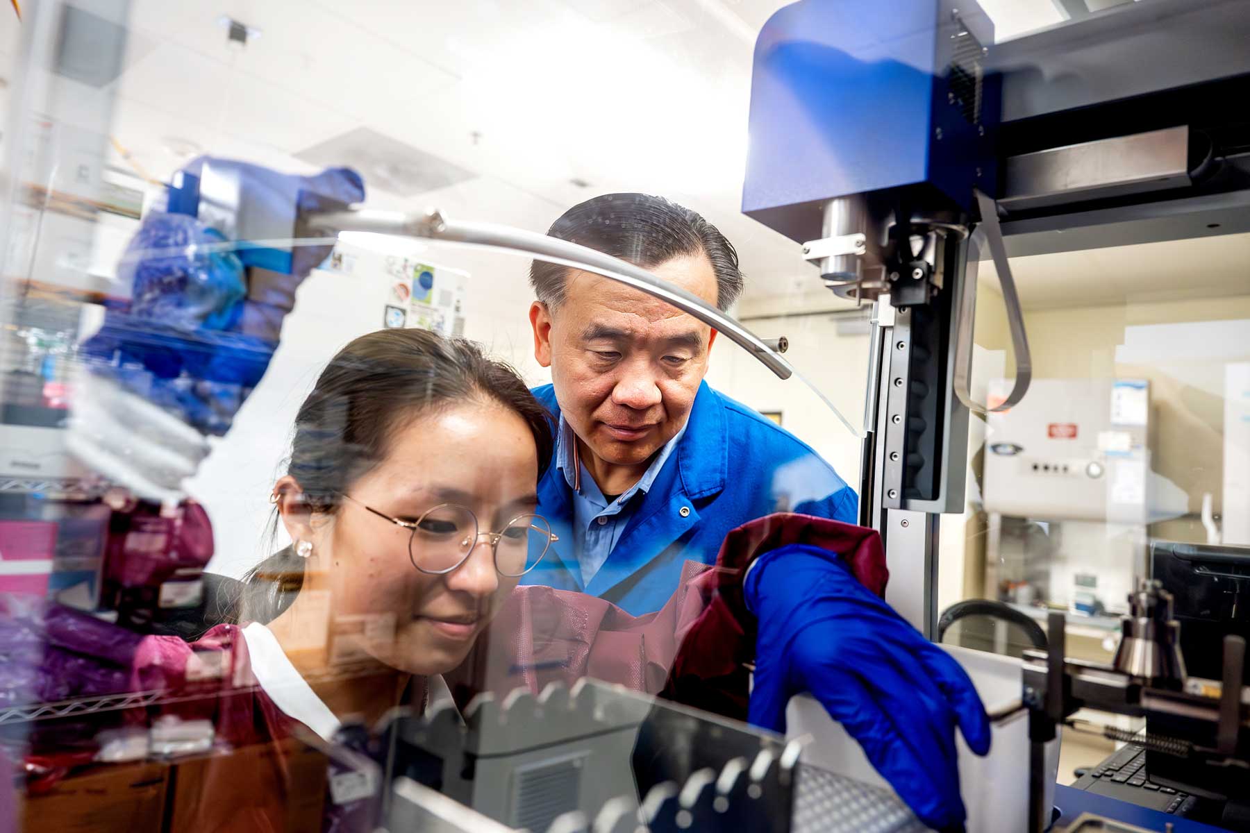 Charles Chiu and Jenna Chiu wear protective lab gear as Jenna pipes DNA samples into a machine.