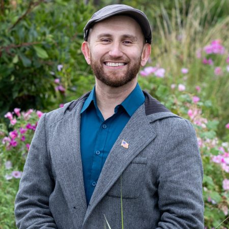 Jonathan smiles wearing grey coat and dress shirt.