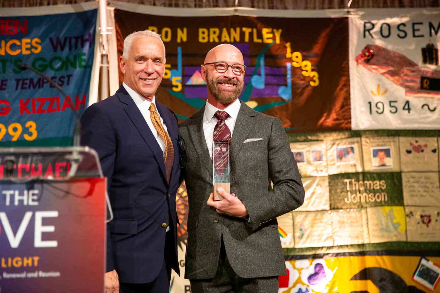 Dan Bernal smiles as he holds his award and stands next to John Cunningham onstage.