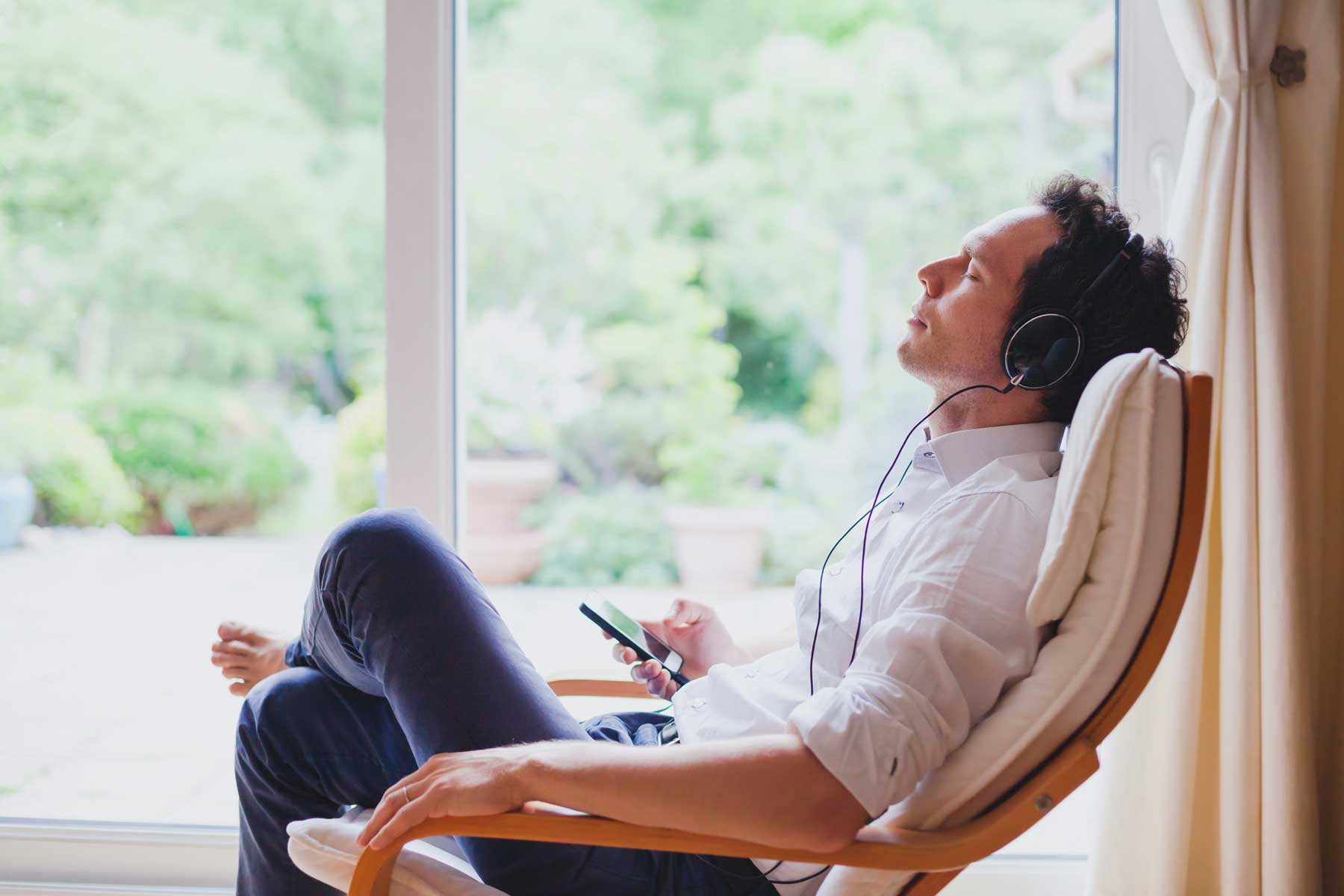 A man wearing headphones and office attire relaxes and meditates on a chair.