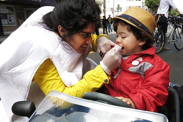 Zarah Ahmed, dressed in a tooth costume, applies a fluoride treatment to a little boy