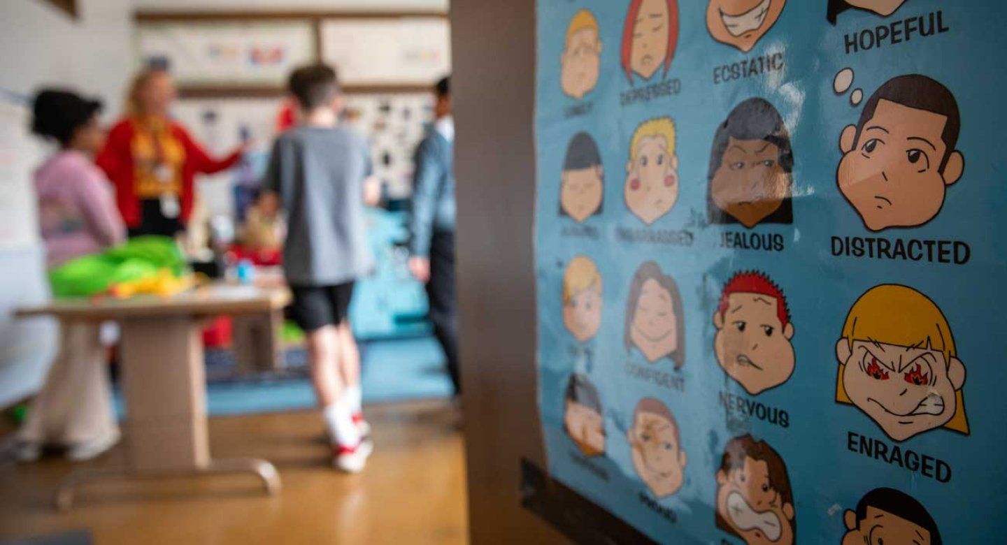 A classroom door features a poster with children's faces that represnent emotions. Inside the classroom, a social worker and children do activities to help manage A D H D.