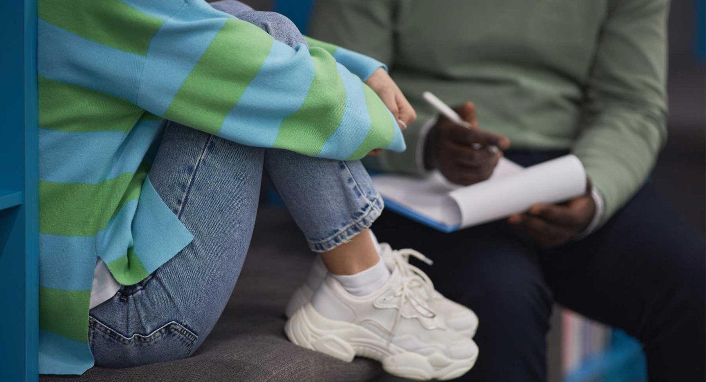 A therapist takes notes while they speak with a young patient.