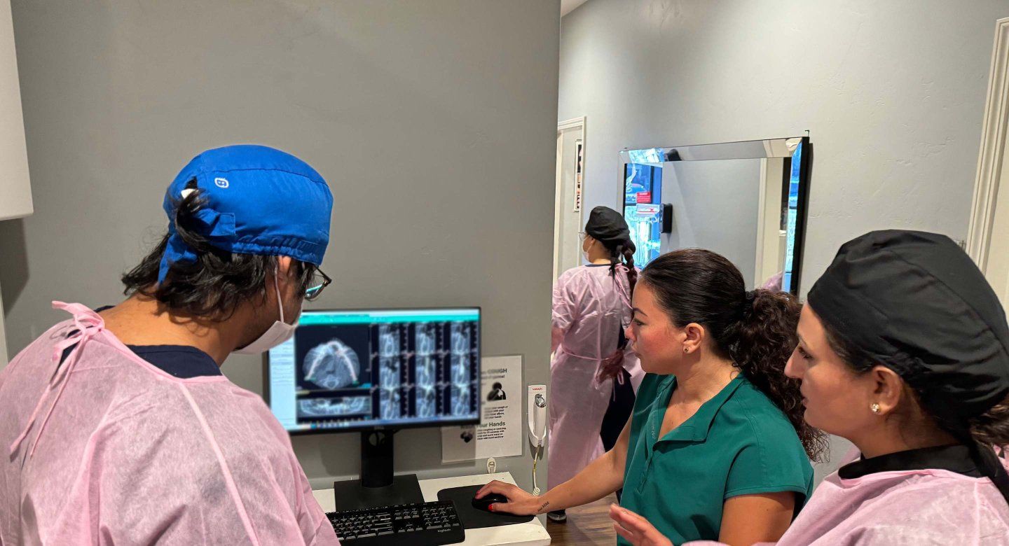 three dental staff in office look over x rays pensively.