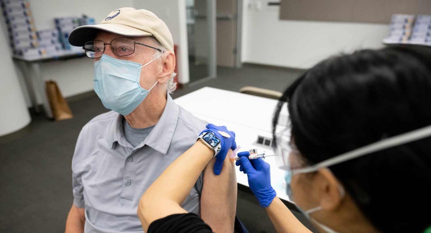 An elderly man wearing a mask receives a vaccine from a medical professional.