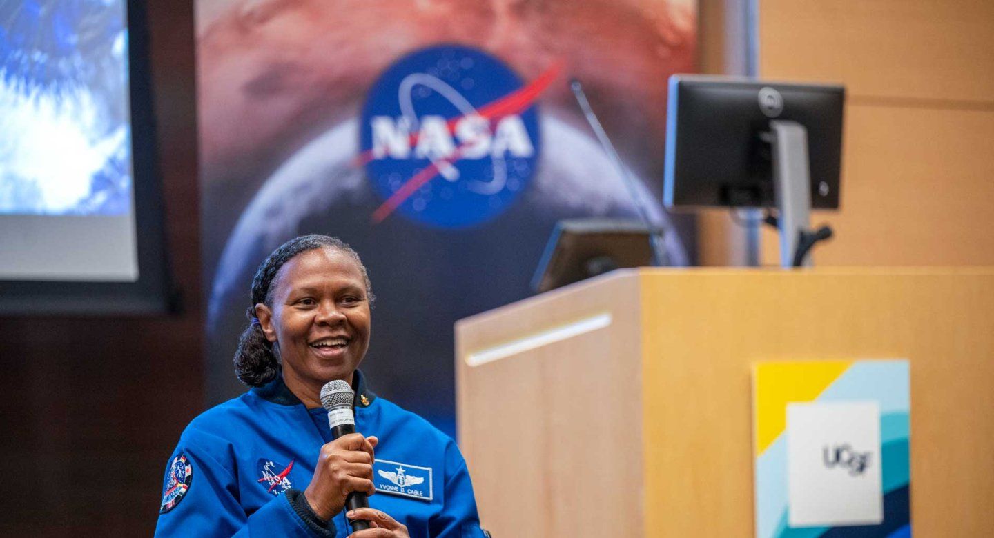 NASA astronaut Yvonne Cagle speaks at UCSF. In the background are banners featuring the NASA and UCSF logos.