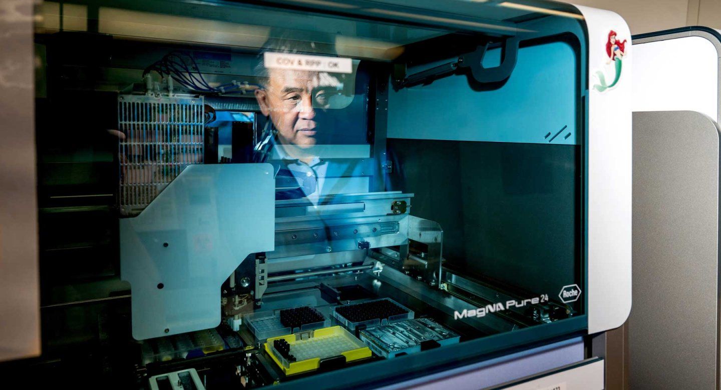 Researcher Charles Chiu is pictured in the reflection of a robotic machine used to extract DNA from a sample.