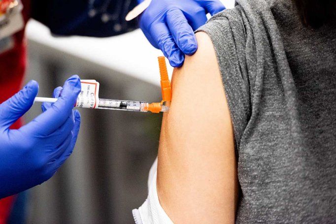 A health professional wearing a blue latex gloves delivers a COVID-19 vaccine in to a patient's shoulder.