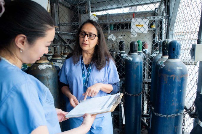 Two people talk and hold a clipboard while surrounded by nitrous oxide tanks.