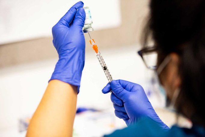 A pharmacy technician wearing blue latex glove and a surgical mask prepares a dose of the Moderna COVID-19 vaccine.