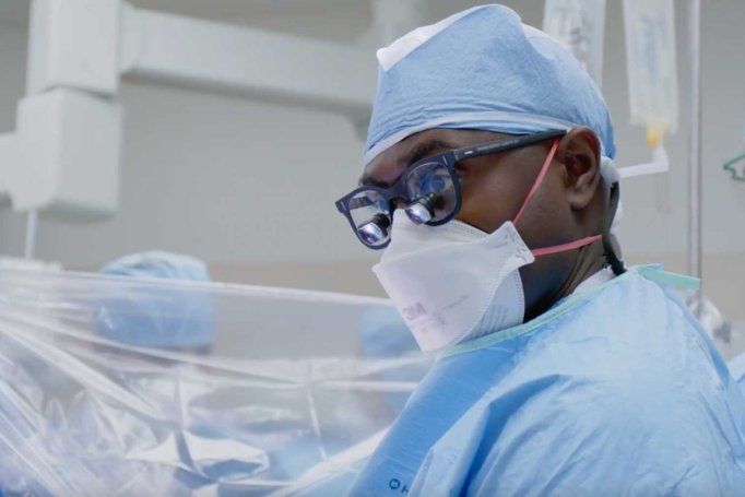 Neuroseurgon Shawn Hervey-Jumper wears surgical scrubs and a mask, along with surgical loupes, while he performs neurosurgery.