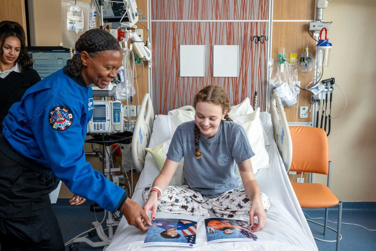 NASA astronaut Yvonne Cagle gives a signed photo to a young girl who is a patient at U C S F Benioff Children's Hospital San Francisco. Both smile as the girl admires the photo.