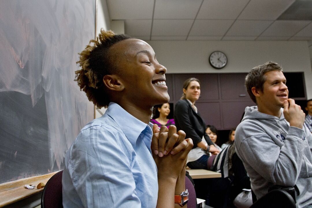 Chemtai Mungo clasps her hands and smiles in a classroom full of fellow students.