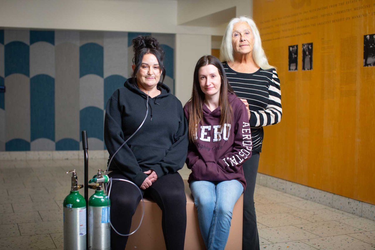 Two sisters, one of whom uses an oxygen tank to breathe due to the COPA disease, stand with their mother Betty.