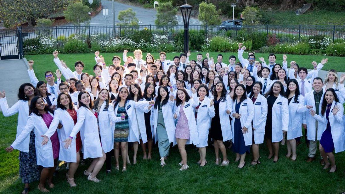 group of festive students in white lab coats smile.