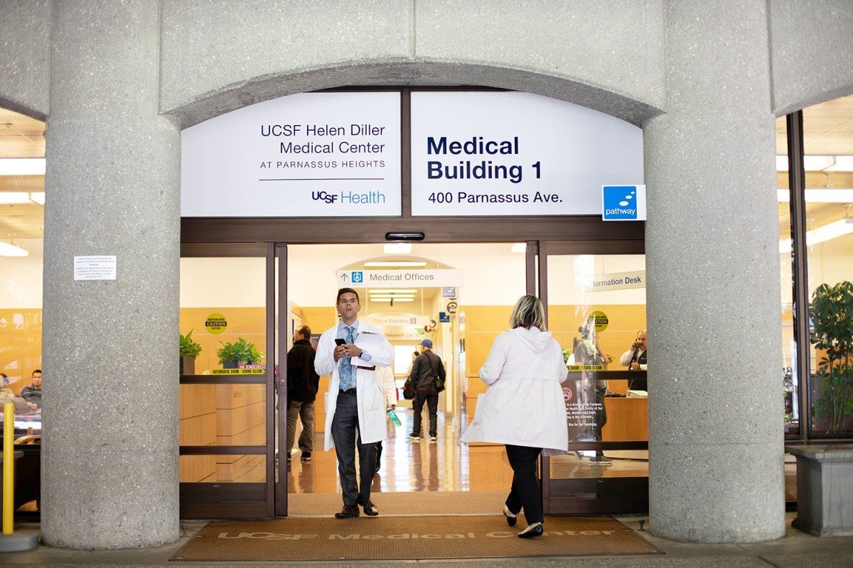 people walking in and out of the UCSF Helen Diller Medical Center at Parnassus Heights. UCSF logo is visible in the photo as well as the full address Medical building 1 at 400 Parnassus Ave 