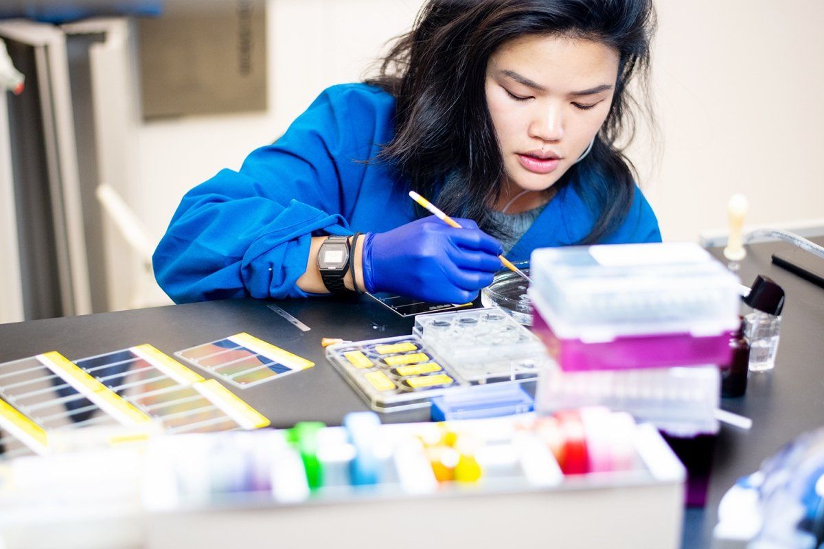 A woman in blue lab coat looking into Petri dish