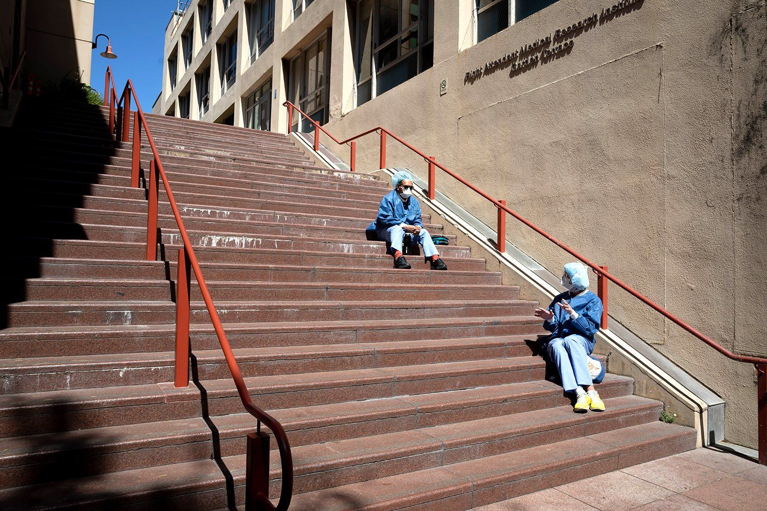 Two surgical technicians sit apart on the steps of the Parnassus Campus as they eat lunch