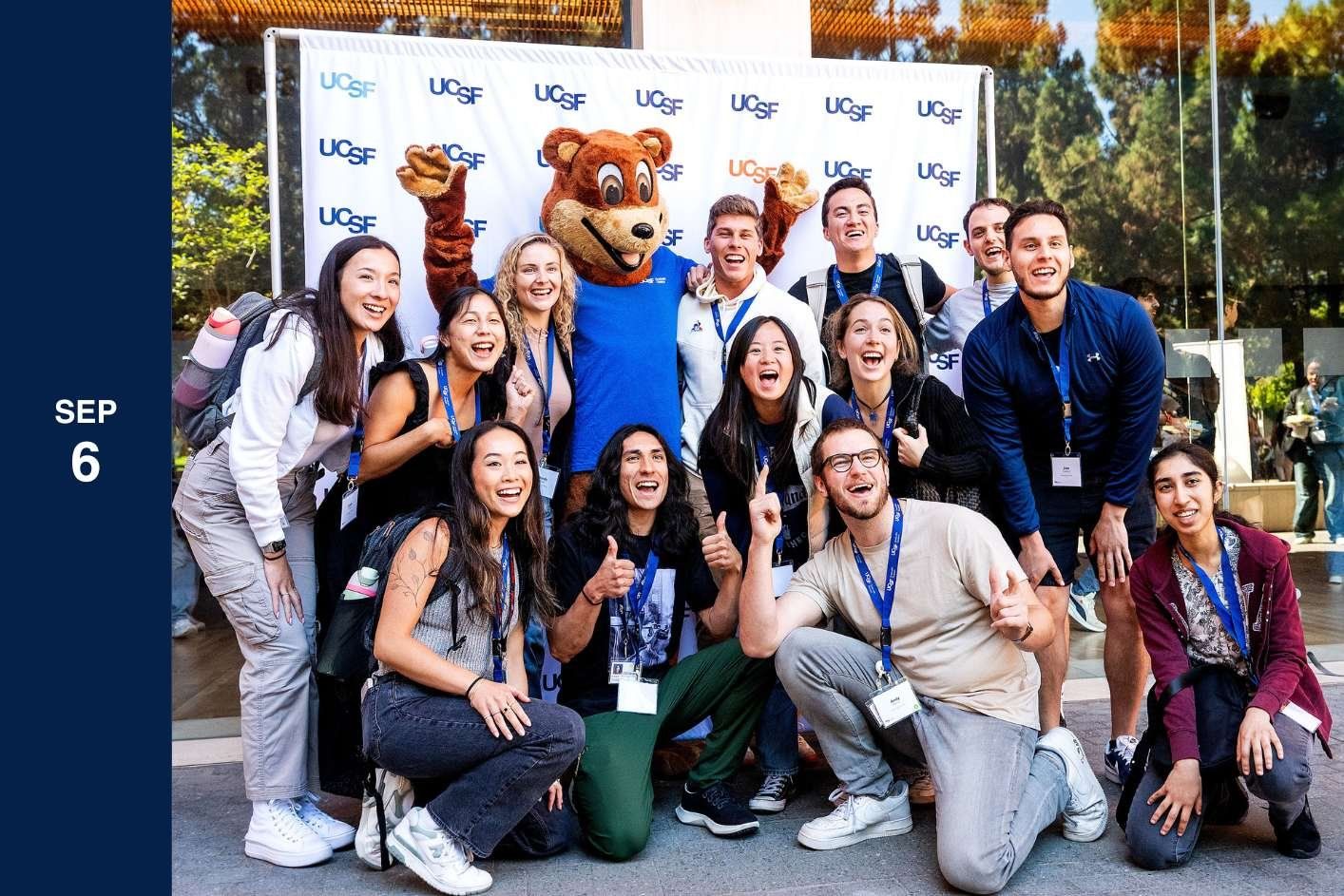 group of students pose with bear on step and repeat.