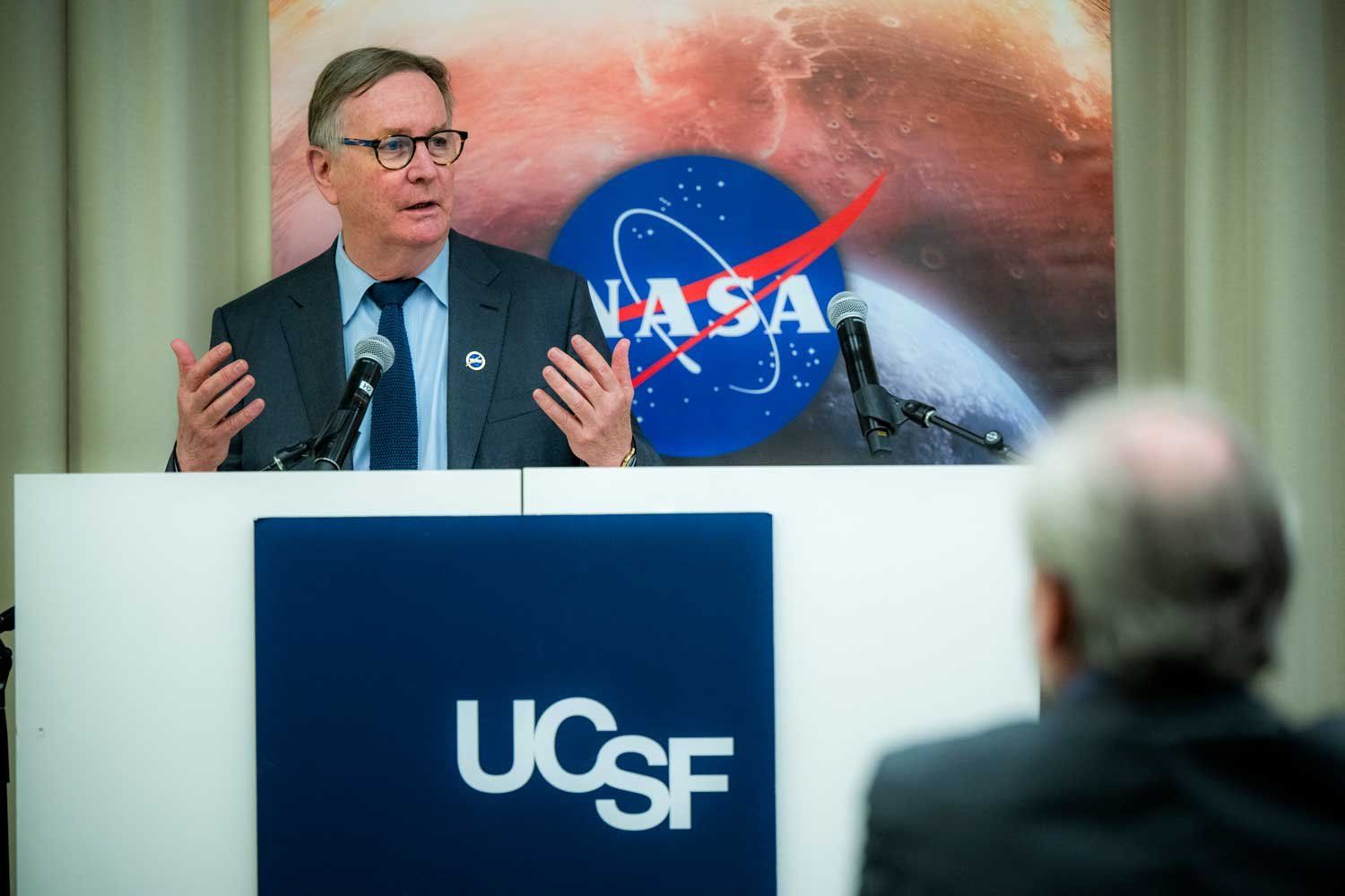 UCSF Chancellor Sam Hawgood speaks at UCSF. In the background are banners featuring the NASA and UCSF logos.