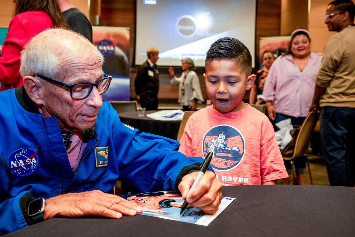 NASA astronaut Kenneth “Taco” Cockrell signs an autograph on a photo for a young boy who is excited to meet an astronaut.