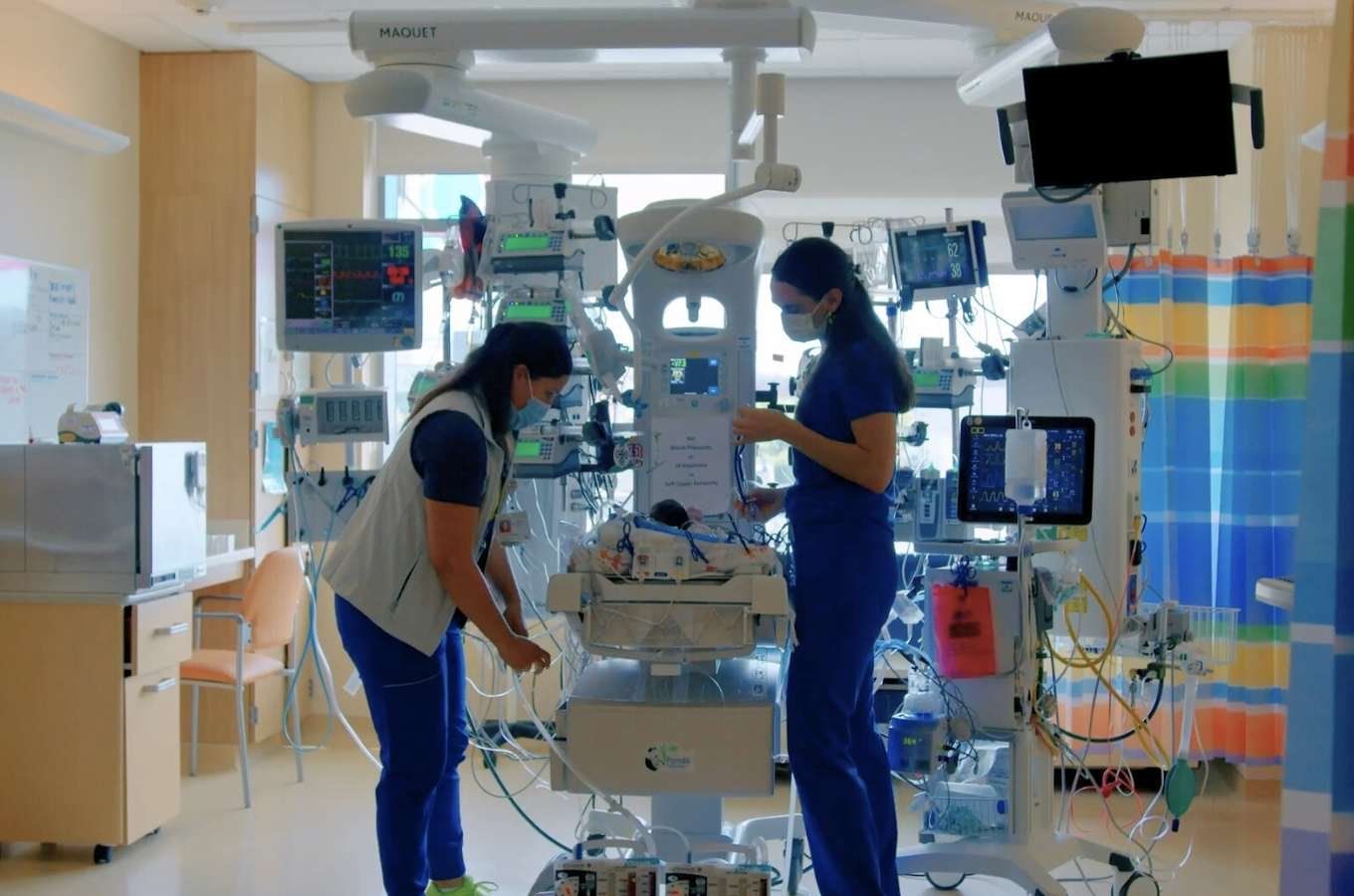 Two nurses calibrate a machine in empty hospital room.