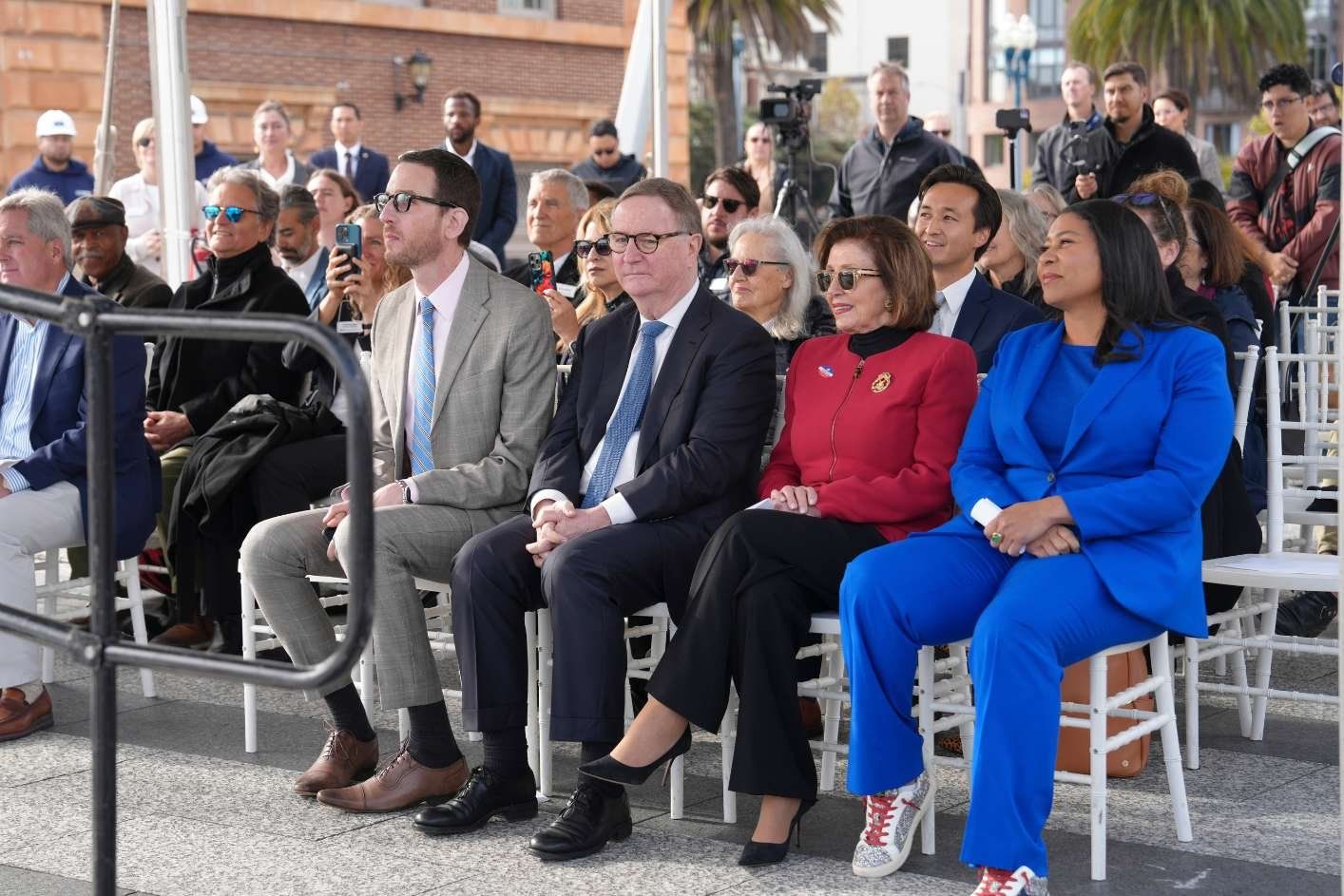 Sam Hawgood sits next to Nancy Pelosi in outdoor seating at ferry landing reception.