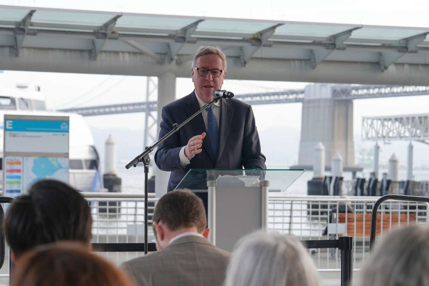 Chancellor Sam Hawgood at podium at a ferry landing speaks to seated crowd.