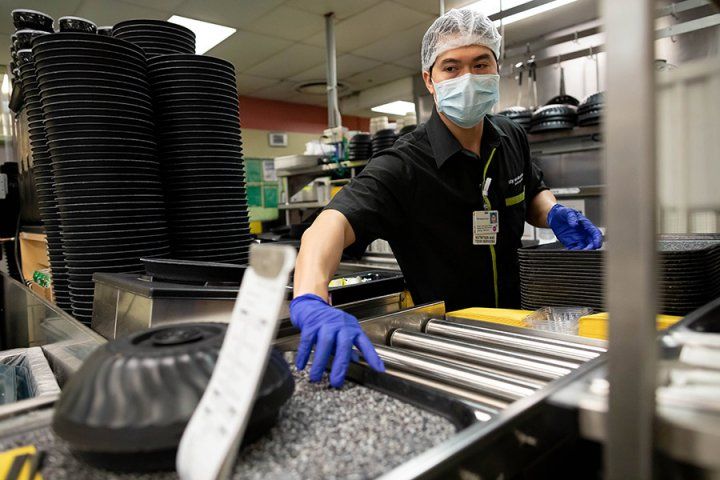 Food services worker grabs a tray while wearing protective gear