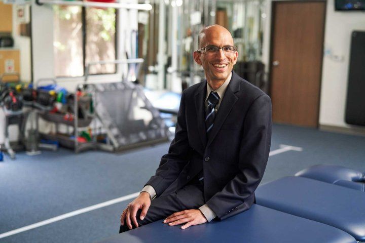 Nirav Pandya, MD, sits on a bench in an exercise and physical therapy room.
