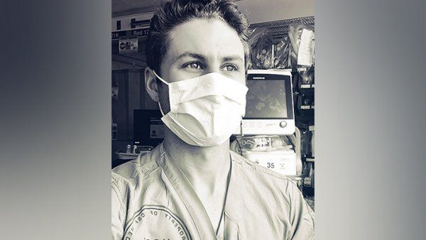 Portrait of Max Rausch in scrubs and a face mask at the hospital.