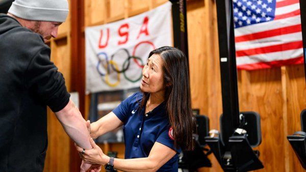 Ben Davison, left, receives physical therapy on his arm from Dr. Cindy Cang, right. On a wall in the background are an American flag and a Team USA Olympic flag.